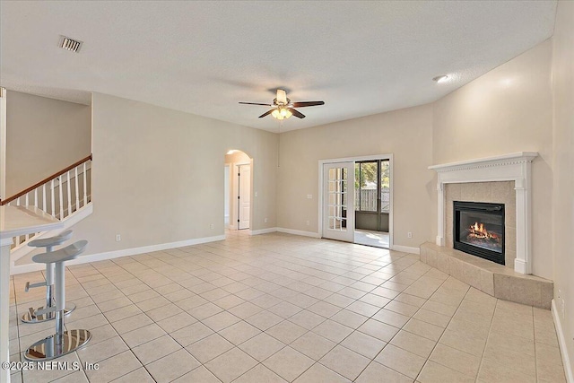 unfurnished living room featuring light tile patterned flooring, ceiling fan, a tiled fireplace, and a textured ceiling