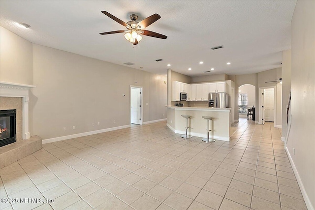 unfurnished living room with light tile patterned flooring, ceiling fan, a tiled fireplace, and a textured ceiling