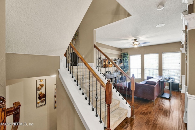 stairway with hardwood / wood-style flooring, a textured ceiling, and ceiling fan