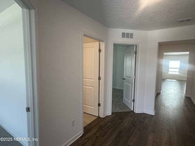 hall featuring baseboards, dark wood-style floors, visible vents, and a textured ceiling