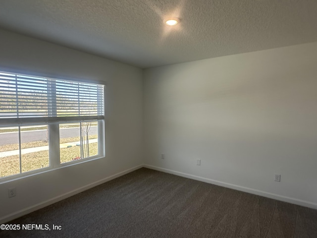 empty room with a textured ceiling, baseboards, and dark colored carpet