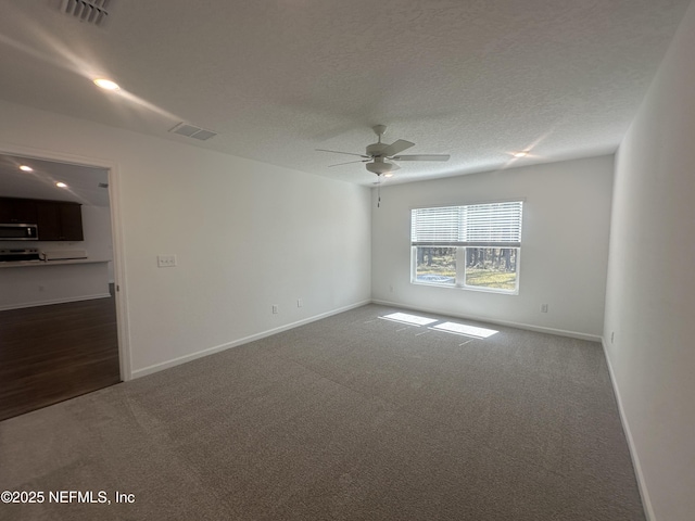 unfurnished room with dark colored carpet, visible vents, baseboards, and a textured ceiling