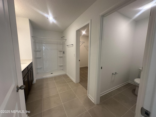 bathroom featuring a stall shower, a textured ceiling, a walk in closet, tile patterned floors, and toilet