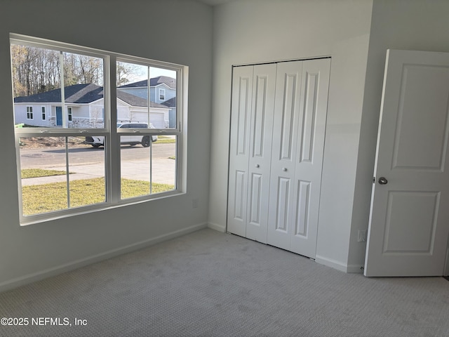 unfurnished bedroom with carpet, a residential view, baseboards, and a closet