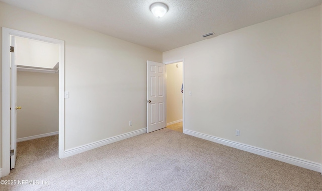 unfurnished bedroom with a closet, a spacious closet, light carpet, and a textured ceiling