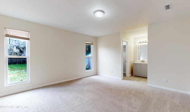 unfurnished bedroom with light colored carpet, sink, and multiple windows