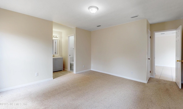 unfurnished bedroom featuring light carpet and ensuite bath