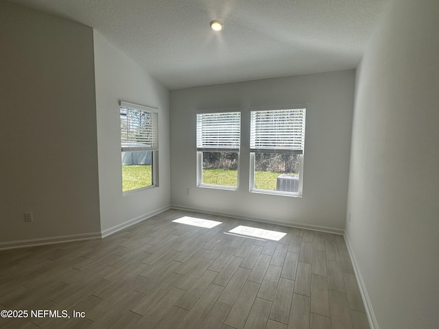 empty room featuring baseboards, a textured ceiling, lofted ceiling, and wood finished floors