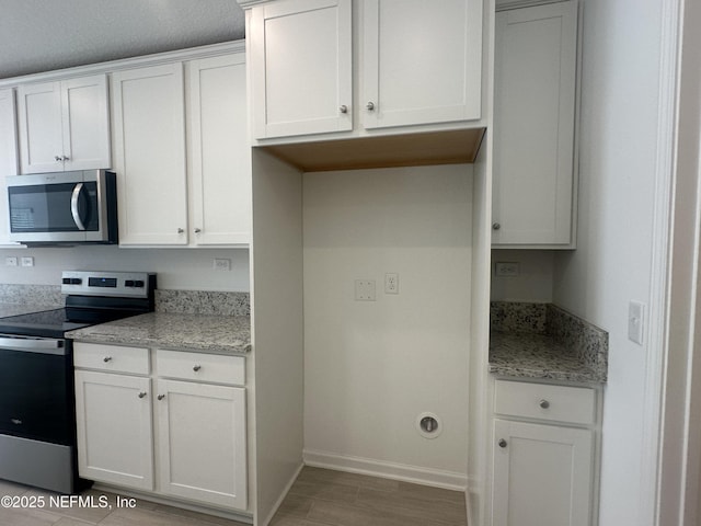 kitchen featuring baseboards, light stone counters, stainless steel appliances, light wood-style floors, and white cabinetry