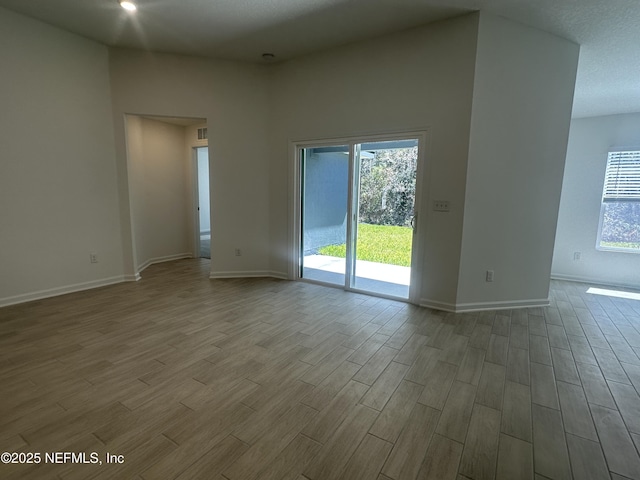 empty room featuring recessed lighting, wood finished floors, baseboards, and a wealth of natural light