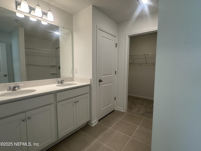 bathroom with a walk in closet, tile patterned floors, double vanity, and a sink