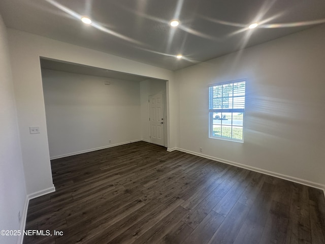 spare room with baseboards and dark wood-style flooring