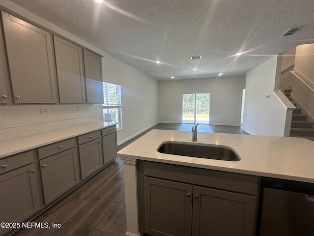 kitchen featuring open floor plan, dark wood-style flooring, gray cabinets, stainless steel dishwasher, and a sink