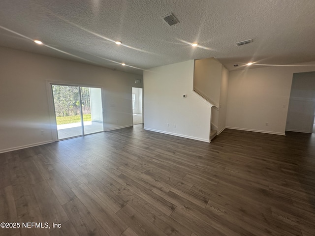 spare room featuring a textured ceiling, visible vents, dark wood-style flooring, and baseboards