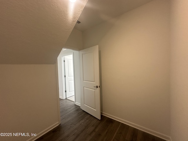 additional living space with dark wood finished floors, a textured ceiling, baseboards, and vaulted ceiling