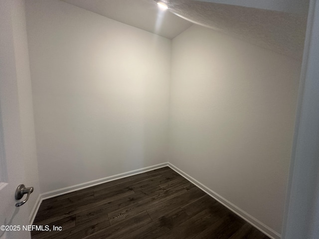 unfurnished room with dark wood-style floors, a textured ceiling, lofted ceiling, and baseboards