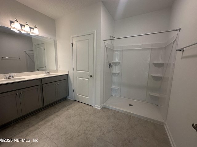 bathroom featuring double vanity, a walk in shower, a textured ceiling, and a sink