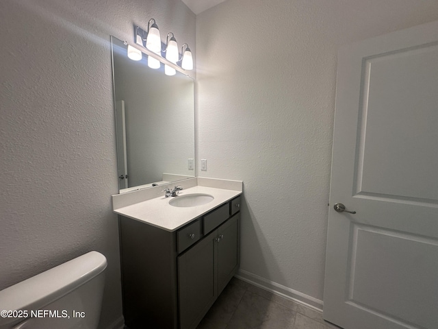 half bath featuring tile patterned floors, toilet, vanity, and a textured wall