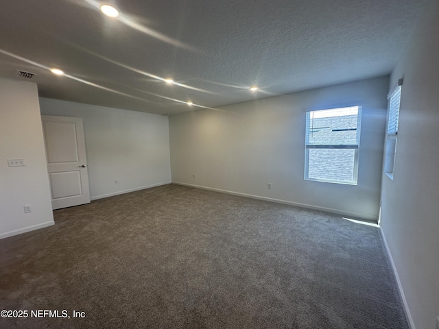 unfurnished room featuring visible vents, baseboards, dark colored carpet, and a textured ceiling