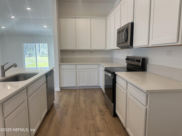 kitchen featuring wood finished floors, recessed lighting, a sink, appliances with stainless steel finishes, and white cabinetry