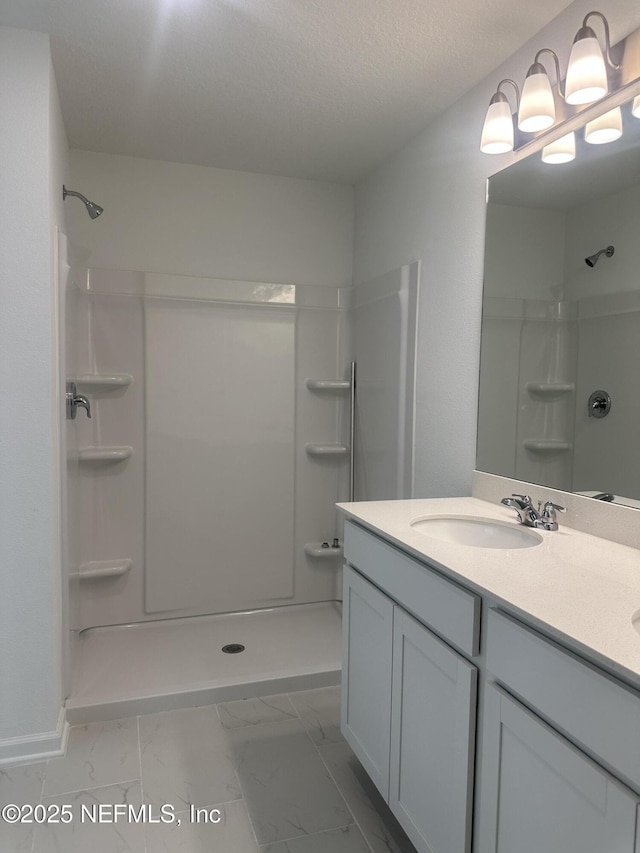 full bathroom featuring marble finish floor, a textured ceiling, vanity, and walk in shower