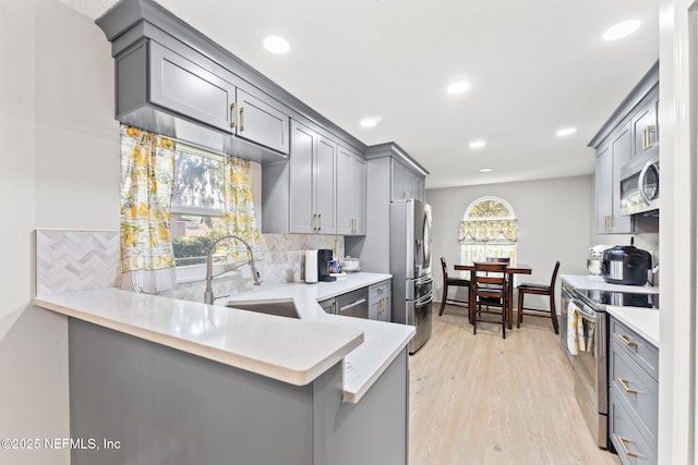 kitchen with stainless steel appliances, kitchen peninsula, sink, and gray cabinetry