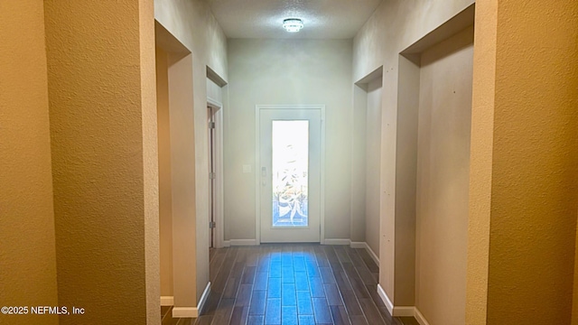 entryway with a textured wall, dark wood-type flooring, and baseboards