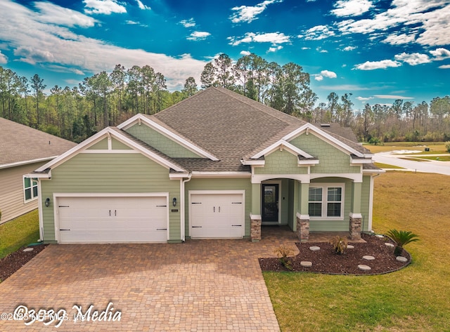 craftsman inspired home with an attached garage, roof with shingles, decorative driveway, and a front yard