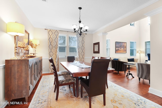 dining space with ornamental molding, a chandelier, light hardwood / wood-style floors, and ornate columns