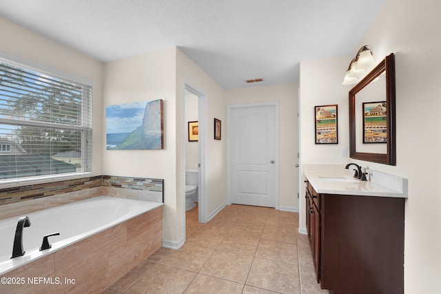 bathroom with vanity, toilet, tiled tub, tile patterned floors, and a textured ceiling