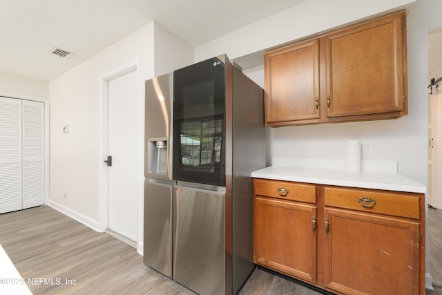 kitchen featuring stainless steel fridge, light hardwood / wood-style floors, and a textured ceiling