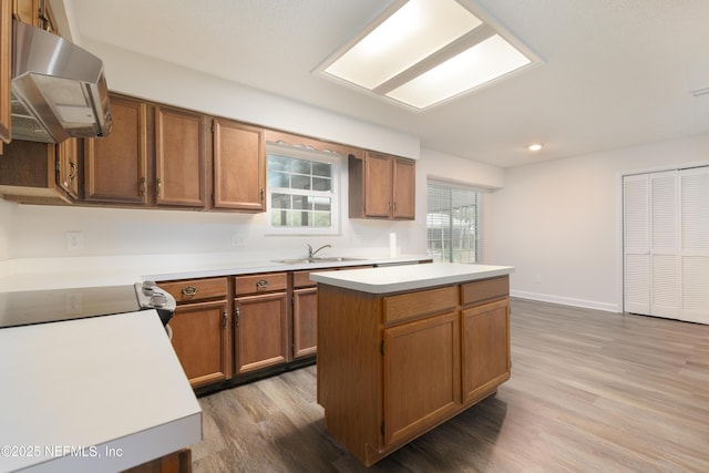 kitchen with a kitchen island, stainless steel stove, sink, wall chimney range hood, and light hardwood / wood-style flooring