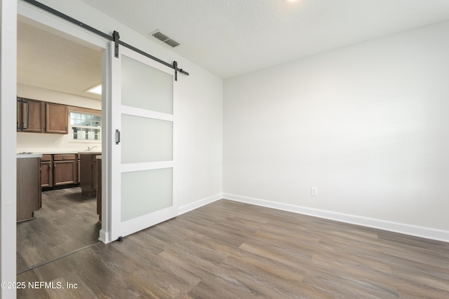 spare room featuring dark hardwood / wood-style floors, a barn door, sink, and a textured ceiling