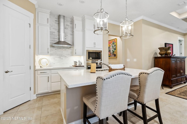 kitchen with decorative light fixtures, built in microwave, white cabinetry, wall chimney range hood, and a center island with sink