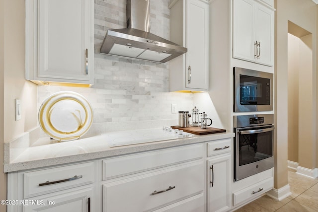 kitchen with built in microwave, light stone countertops, wall chimney range hood, oven, and white cabinets