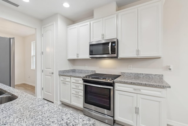 kitchen featuring appliances with stainless steel finishes, white cabinets, and light stone counters