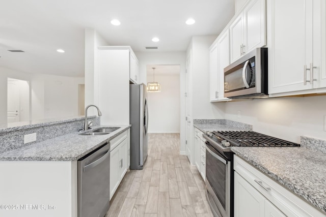 kitchen with sink, light hardwood / wood-style flooring, appliances with stainless steel finishes, light stone countertops, and white cabinets