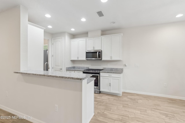 kitchen with light hardwood / wood-style flooring, appliances with stainless steel finishes, white cabinetry, light stone counters, and kitchen peninsula