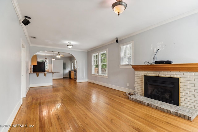 unfurnished living room with ornamental molding, a brick fireplace, hardwood / wood-style floors, and ceiling fan