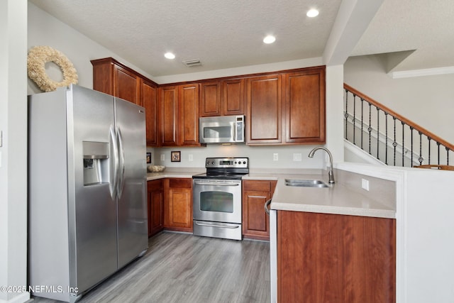 kitchen with appliances with stainless steel finishes, sink, a textured ceiling, and light wood-type flooring