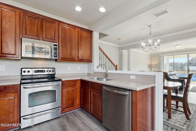 kitchen with sink, hanging light fixtures, ornamental molding, kitchen peninsula, and stainless steel appliances