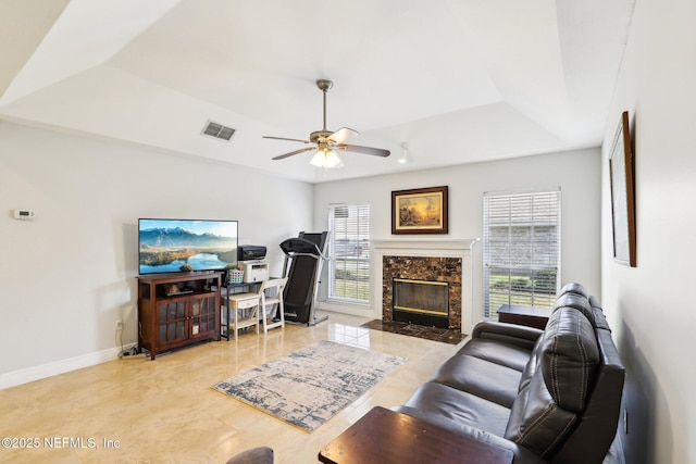 living room featuring baseboards, visible vents, a raised ceiling, a ceiling fan, and a fireplace