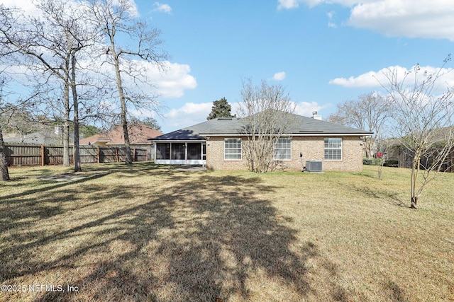 rear view of property with a sunroom, a fenced backyard, a yard, central air condition unit, and brick siding