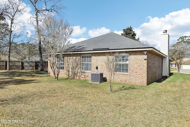 back of house with central AC, brick siding, fence, a lawn, and a chimney