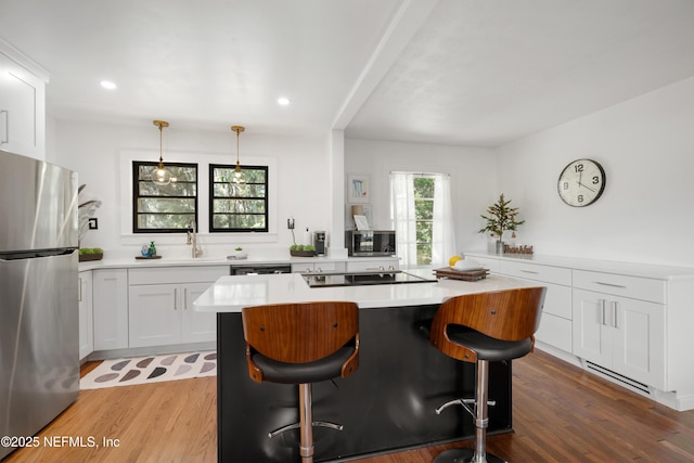 kitchen with pendant lighting, white cabinets, a kitchen bar, a center island, and black appliances