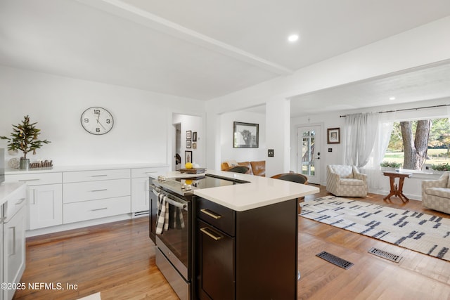 kitchen featuring dark brown cabinets, light hardwood / wood-style floors, an island with sink, white cabinets, and stainless steel electric range oven