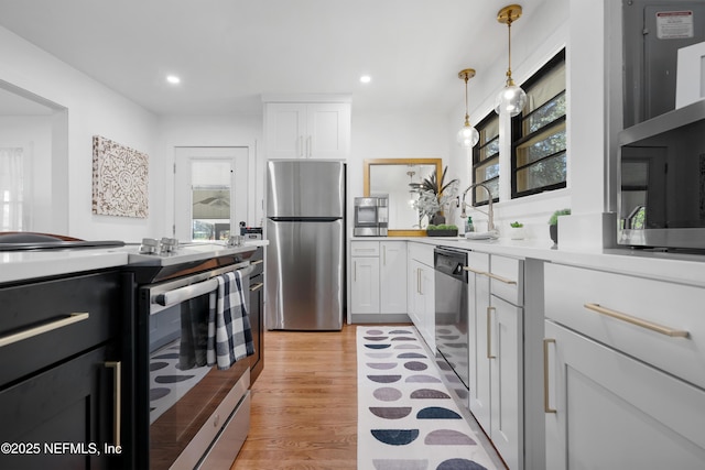 kitchen with sink, light hardwood / wood-style flooring, hanging light fixtures, appliances with stainless steel finishes, and white cabinets