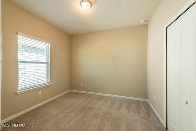 unfurnished bedroom featuring light colored carpet, a textured ceiling, and a closet