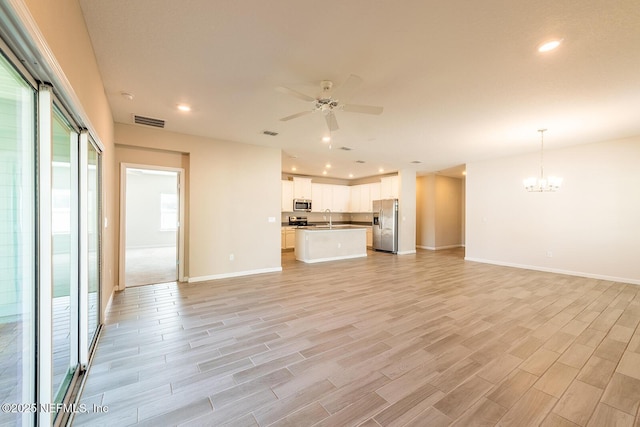 unfurnished living room with sink, ceiling fan with notable chandelier, and light wood-type flooring