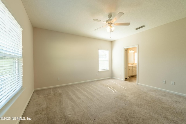 unfurnished bedroom featuring connected bathroom, light colored carpet, a textured ceiling, and ceiling fan